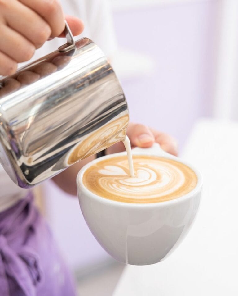 Barista pouring latte art into a white cup